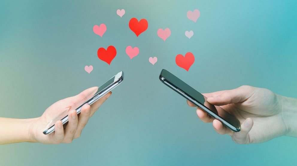 Boy and Girls hands each holding a phone. Texting one another with pink and red hearts floating up from the phones.